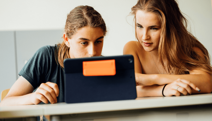 Ein Schüler und eine Schülerin blicken gemeinsam auf den Bildschirm eines Tablets.