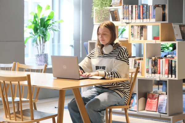 Eine Frau sitzt vor einem Bücherregal an einem Laptop
