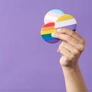 Eine Hand mit 3 Pride-Buttons in der Hand vor violettem Hintergrund.