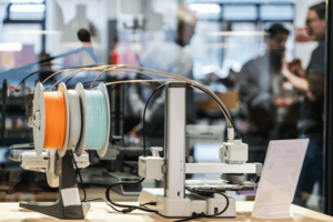 Im Vordergrund ist ein Gerät des Makerlab, im Hintergrund sind verschwommen einige Menschen zu sehen