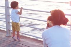 junger Mensch schaut aufs Meer und wird von älterem Menschen mit einem Smartphone fotografiert