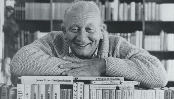 Schwarz-Weiß-Bild von James Krüss auf einem Stapel Bücher.