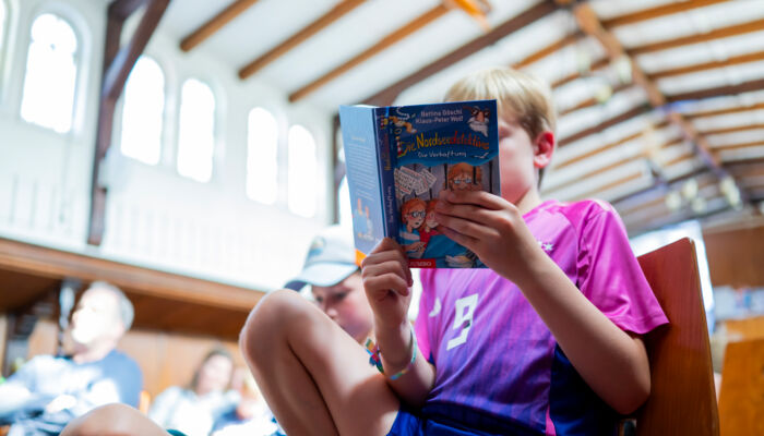 Impression Flussschifferkirche: ein Junge liest aus einem Kinderbuch. Im Hintergrund unscharf zu erkennen: die Decke der Flusschifferkirche.