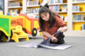 Kind sitzt auf Boden in Bücherhalle und blättert in einem Buch