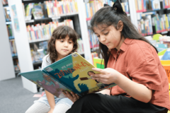 Zwei Kinder sitzen in Bücherhalle und lesen in Buch