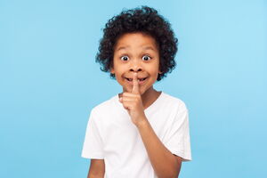 Kind, das als Zeichen zum Leisesein einen Finger an die Lippen legt