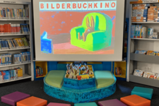 Eine Leinwand mit dem Slogan "Bilderbuchkino", davor bunte Sitzkissen