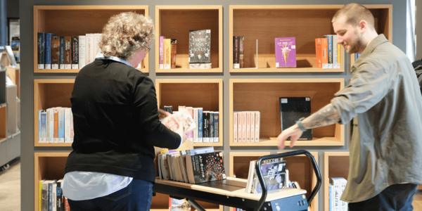 zwei Bibliotheksmitarbeitende stellen Bücher ein