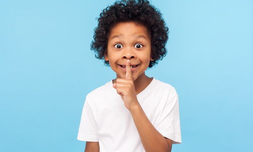 Kind, das als Zeichen zum Leisesein einen Finger an die Lippen legt