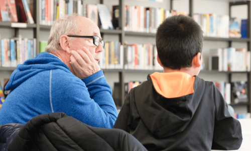 Mann hilft Kind beim Lesen lernen in der Bücherhalle