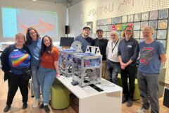Acht Personen neben zwei 3D-Druckern auf einem Tisch