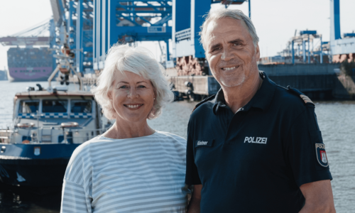 Ältere Frau und älterer Mann in Polizeiuniform stehen am Hamburger Hafen