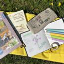 Ein gelbes Tuch auf einer Wiese. Darauf liegen Bücher und Stifte.
