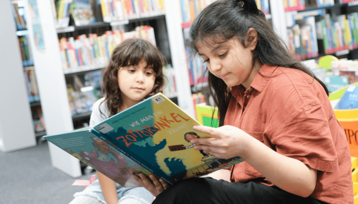Zwei Kinder sitzen in Bücherhalle und lesen in Buch