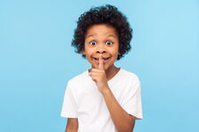 Kind, das als Zeichen zum Leisesein einen Finger an die Lippen legt