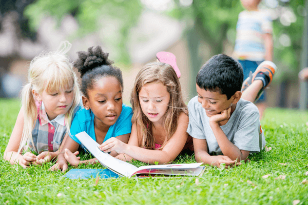 4 lesende Kinder im Gras