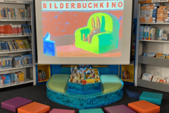 Leinwand, auf der ein Vorschaubild vom Bilderbuchkino zu sehen ist, und davor bunte Sitzkissen
