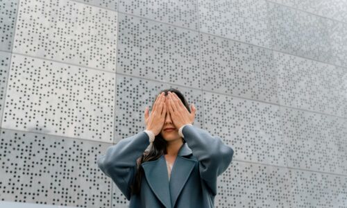 Eine Frau hält sich die Augen zu vor einer Wand mit Brailleschrift
