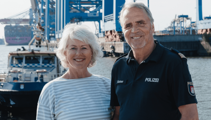 Ältere Frau und älterer Mann in Polizeiuniform stehen am Hamburger Hafen