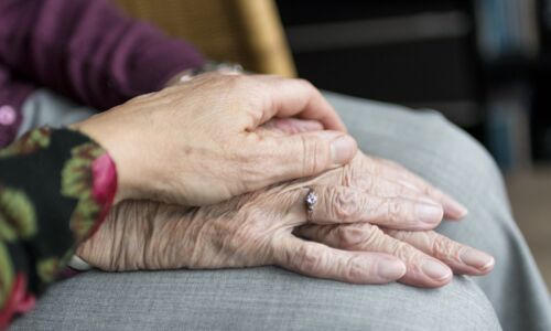 Bild zeigt eine tröstende, unterstützende Hand auf die Hand eines älteren Menschen gelegt