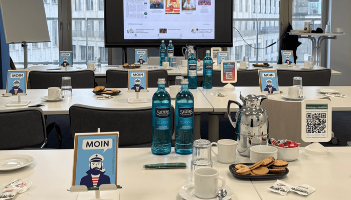 Konferenztische mit Kaffee und Wasser, im Hintergrund ein Bildschirm mit einem ePaper