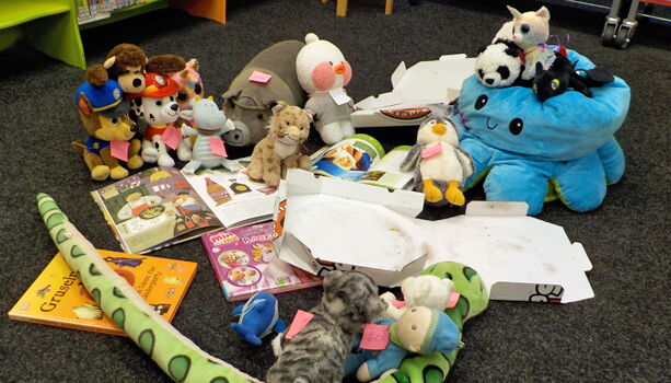 Kuscheltiere umringen aufgeschlagene Bücher und einen leeren Pizzakarton.