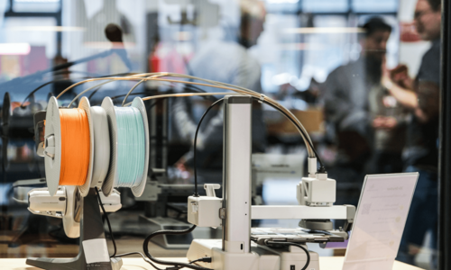 Im Vordergrund ist ein Gerät des Makerlab, im Hintergrund sind verschwommen einige Menschen zu sehen
