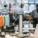 Im Vordergrund ist ein Gerät des Makerlab, im Hintergrund sind verschwommen einige Menschen zu sehen