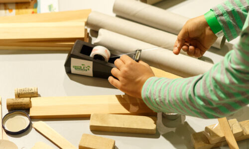 Foto zeigt Person inmitten von Holzklötzen, die an einem Klebeband zieht