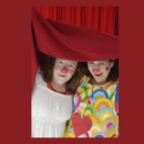 Zwei Frauen, die als Clowns geschminkt sind, schauen unter einem roten Vorhang heraus.