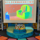Eine Leinwand mit dem Slogan "Bilderbuchkino", davor bunte Sitzkissen