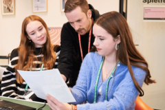 Zwei junge Frauen vor einem Computer bekommen ein Erklärung vom Lehrer