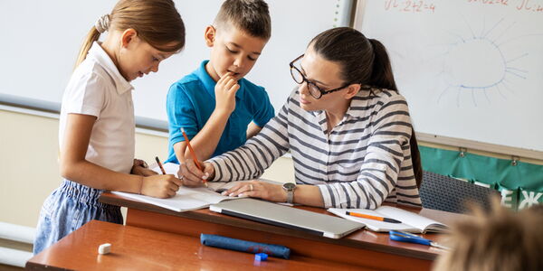 Eine Lehrerin unterrichtet zwei Schulkinder an ihrem Pult