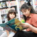 Zwei Kinder sitzen in Bücherhalle und lesen in Buch
