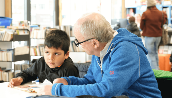 Mann hilft Kind beim Lesen lernen in der Bücherhalle