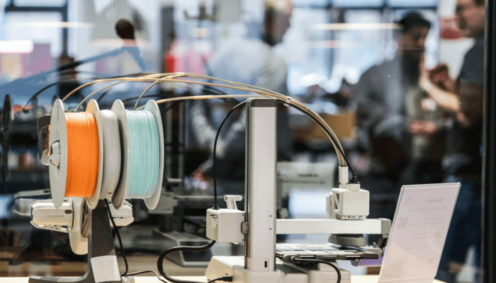 Im Vordergrund ist ein Gerät des Makerlab, im Hintergrund sind verschwommen einige Menschen zu sehen