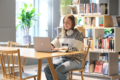Eine Frau sitzt vor einem Bücherregal an einem Laptop