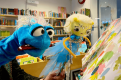 Zwei Plüschhandpuppen mit Bücherregalen im Hintergrund