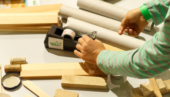 Foto zeigt Person inmitten von Holzklötzen, die an einem Klebeband zieht