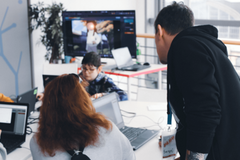 Eine Person blickt einer anderen an einem Scheibtisch mit Laptops über die Schulter
