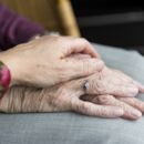 Bild zeigt eine tröstende, unterstützende Hand auf die Hand eines älteren Menschen gelegt