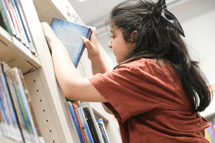 Mädchen stellt Buch in Regal ein