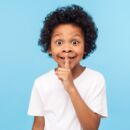 Kind, das als Zeichen zum Leisesein einen Finger an die Lippen legt