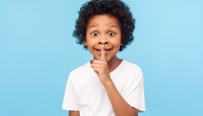 Kind, das als Zeichen zum Leisesein einen Finger an die Lippen legt