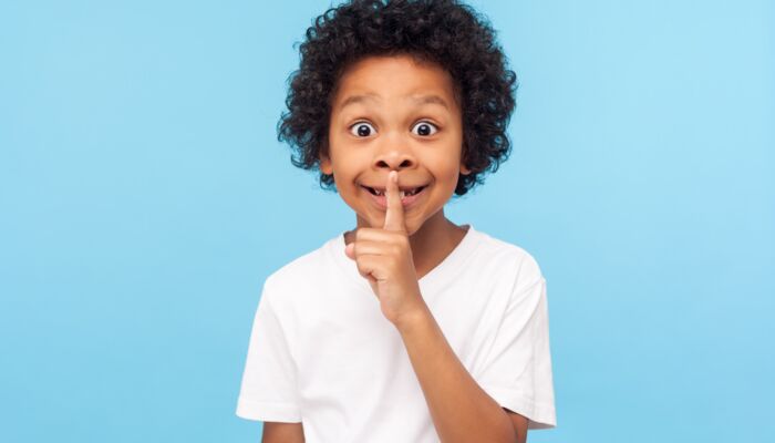 Kind, das als Zeichen zum Leisesein einen Finger an die Lippen legt