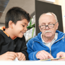 Mann hilft Kind beim Lesen lernen in der Bücherhalle