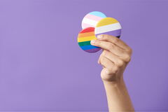 Eine Hand mit 3 Pride-Buttons in der Hand vor violettem Hintergrund.