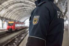 Foto-Bildausschnitt zeigt die Jacke eines Polizisten, der am Bahnhof gegenüber eines Zuges steht