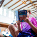 Impression Flussschifferkirche: ein Junge liest aus einem Kinderbuch. Im Hintergrund unscharf zu erkennen: die Decke der Flusschifferkirche.