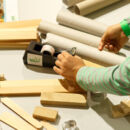 Foto zeigt Person inmitten von Holzklötzen, die an einem Klebeband zieht